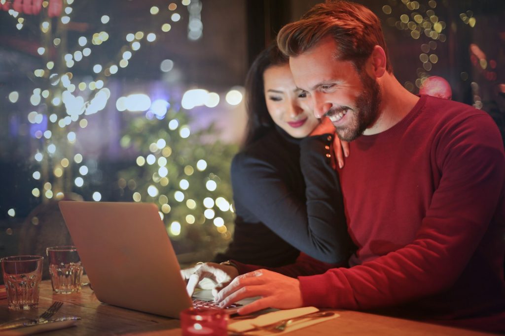 Pareja sonriendo mientras revisa sus finanzas y presupuesto juntos en un portátil