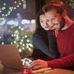 Pareja sonriendo mientras revisa sus finanzas y presupuesto juntos en un portátil
