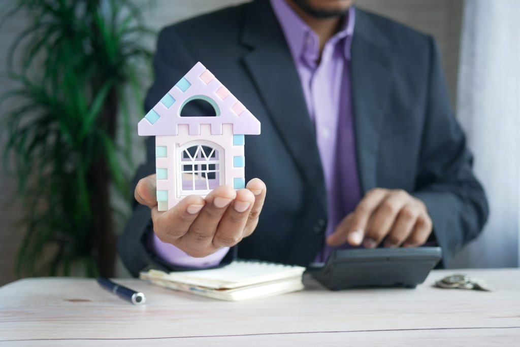 Persona sosteniendo una maqueta de casa junto a una calculadora, haciendo cuentas para decidir si amortizar la hipoteca o invertir sus ahorros
