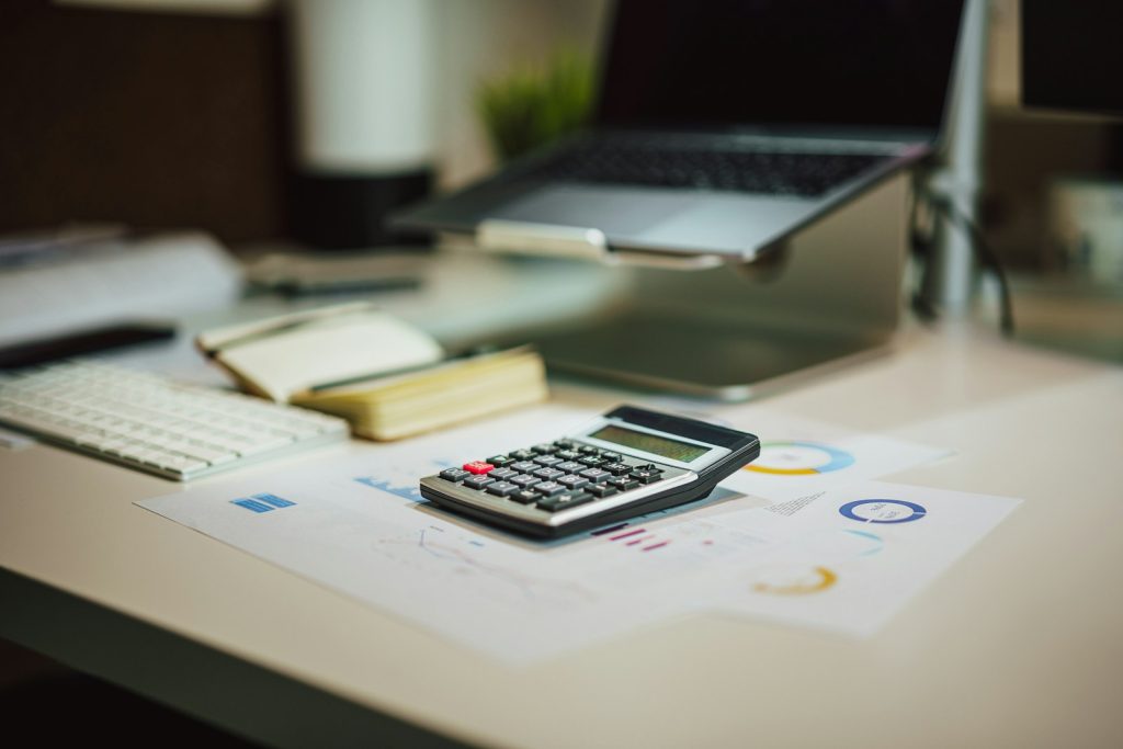 Calculadora sobre una mesa junto a un ordenador portátil, usada para calcular cómo tributan las inversiones en la declaración de la renta