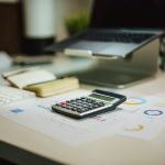 Calculadora sobre una mesa junto a un ordenador portátil, usada para calcular cómo tributan las inversiones en la declaración de la renta